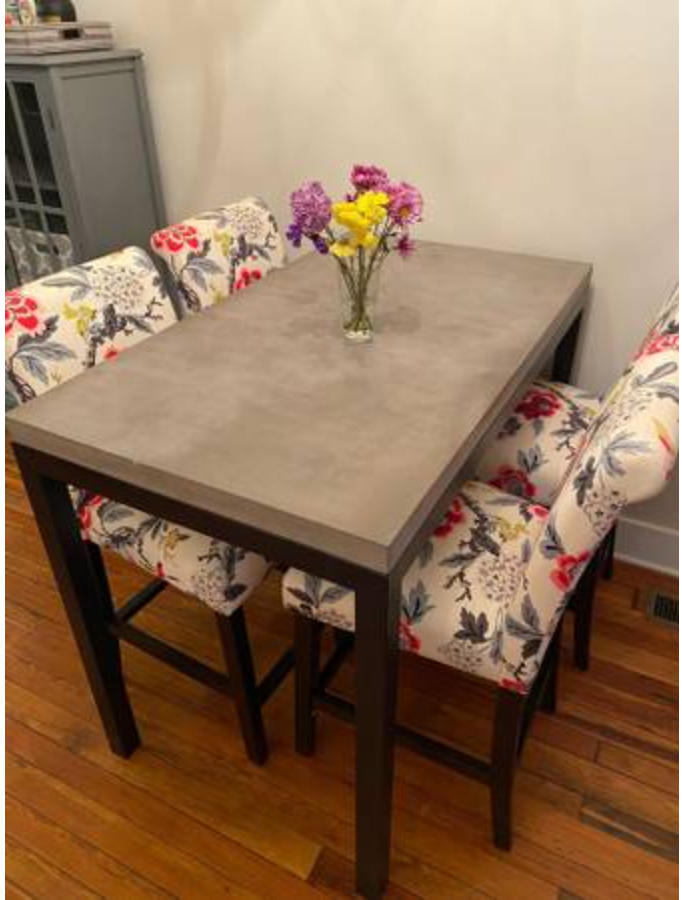 A dinner table with a vase of flowers on it and chairs with floral coverings.